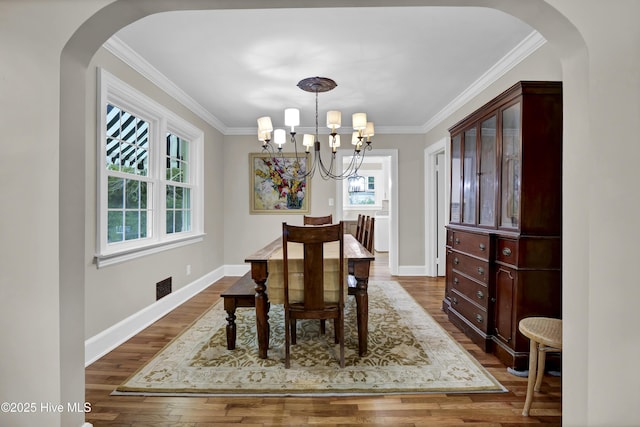 dining space with an inviting chandelier, dark wood-type flooring, crown molding, and visible vents