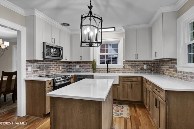 kitchen featuring light countertops, ornamental molding, appliances with stainless steel finishes, an inviting chandelier, and a sink