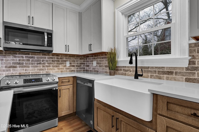 kitchen with a sink, light wood-style floors, appliances with stainless steel finishes, brown cabinetry, and light countertops