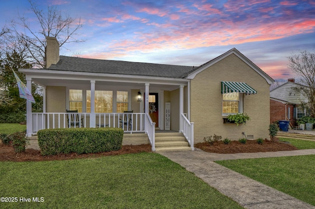 view of front of property featuring a front yard, covered porch, a chimney, crawl space, and brick siding