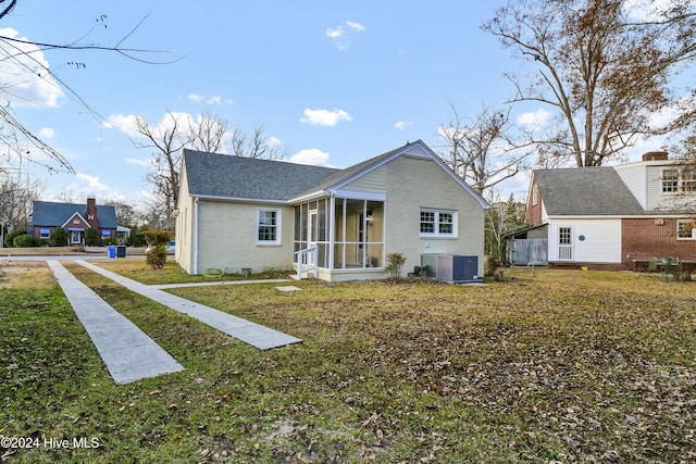 rear view of house featuring a yard, central AC unit, brick siding, and a sunroom