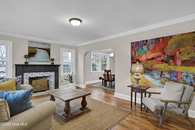 living room with baseboards, a tiled fireplace, ornamental molding, wood finished floors, and arched walkways