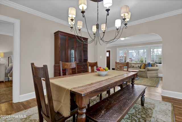 dining space with an inviting chandelier, crown molding, wood finished floors, and arched walkways