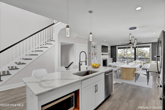 kitchen with pendant lighting, sink, appliances with stainless steel finishes, white cabinetry, and light stone countertops