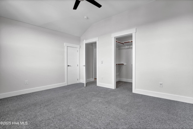 unfurnished bedroom with ceiling fan, a spacious closet, vaulted ceiling, and dark colored carpet