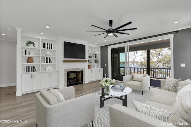 living room featuring crown molding, a large fireplace, ceiling fan, and light wood-type flooring