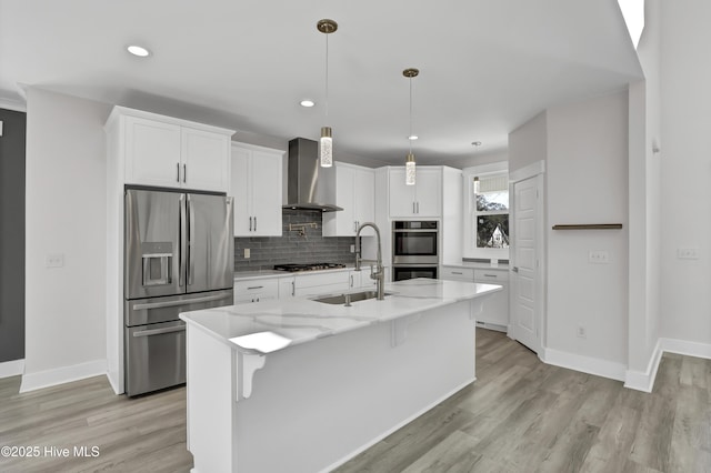 kitchen with sink, white cabinetry, stainless steel appliances, light stone countertops, and wall chimney range hood