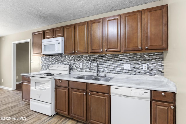 kitchen with white appliances, a sink, light countertops, light wood-type flooring, and backsplash