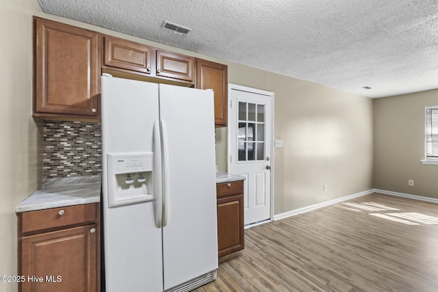 kitchen with tasteful backsplash, light countertops, visible vents, white fridge with ice dispenser, and light wood-type flooring