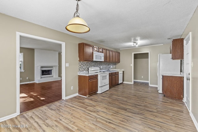 kitchen featuring white appliances, brown cabinetry, open floor plan, light countertops, and pendant lighting