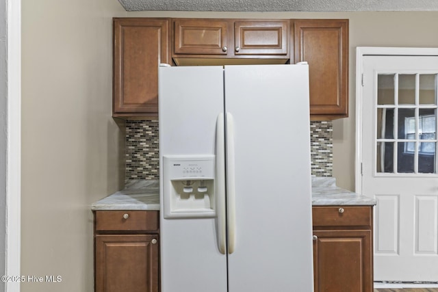 kitchen with light stone countertops, tasteful backsplash, white fridge with ice dispenser, and brown cabinets