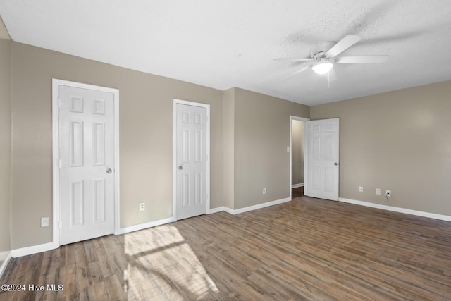 unfurnished bedroom with a textured ceiling, dark hardwood / wood-style flooring, two closets, and ceiling fan