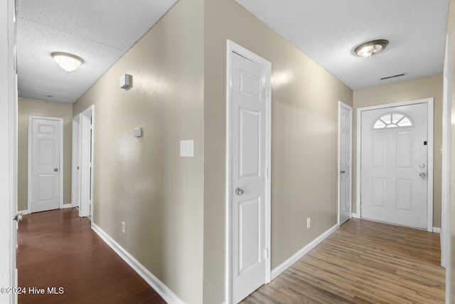 hall with a textured ceiling, wood finished floors, visible vents, and baseboards