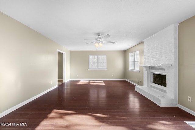 unfurnished living room featuring a ceiling fan, a brick fireplace, dark wood finished floors, and baseboards