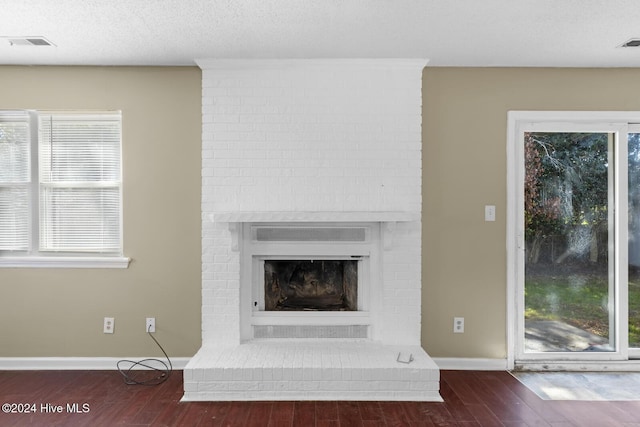 interior details with visible vents, baseboards, wood finished floors, a textured ceiling, and a brick fireplace