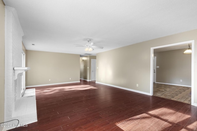 unfurnished living room featuring dark wood-style floors, a fireplace, baseboards, and ceiling fan