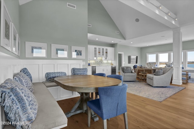 dining area featuring ornate columns, beverage cooler, high vaulted ceiling, light hardwood / wood-style flooring, and sink