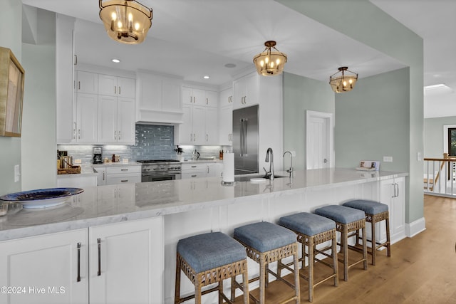 kitchen with white cabinetry, premium appliances, light stone counters, and hanging light fixtures