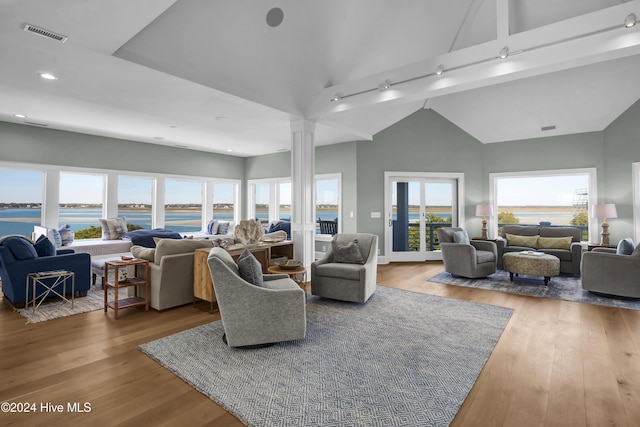 living room featuring a water view, high vaulted ceiling, ornate columns, and hardwood / wood-style floors