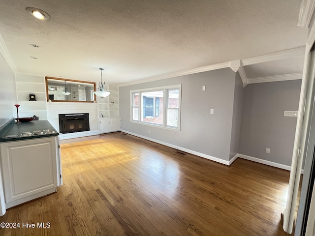 unfurnished living room with a brick fireplace, a textured ceiling, crown molding, built in features, and light hardwood / wood-style flooring