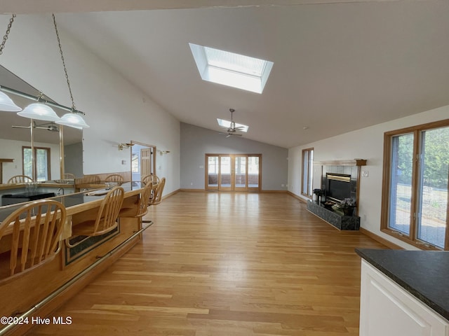 living room featuring ceiling fan, light hardwood / wood-style floors, lofted ceiling with skylight, and a tiled fireplace