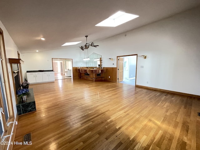 unfurnished living room with ceiling fan, lofted ceiling with skylight, and light hardwood / wood-style flooring