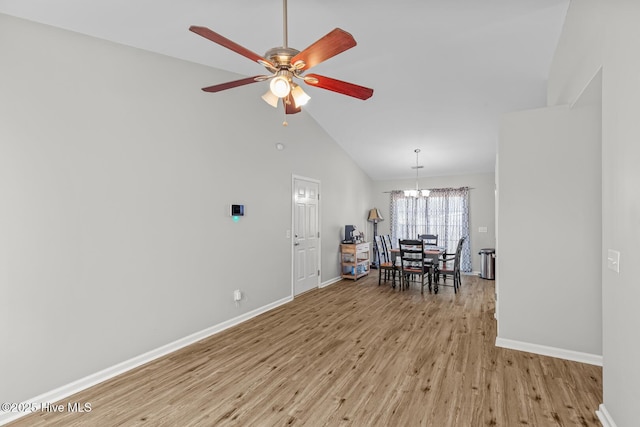 dining room with light wood-type flooring, ceiling fan with notable chandelier, and high vaulted ceiling