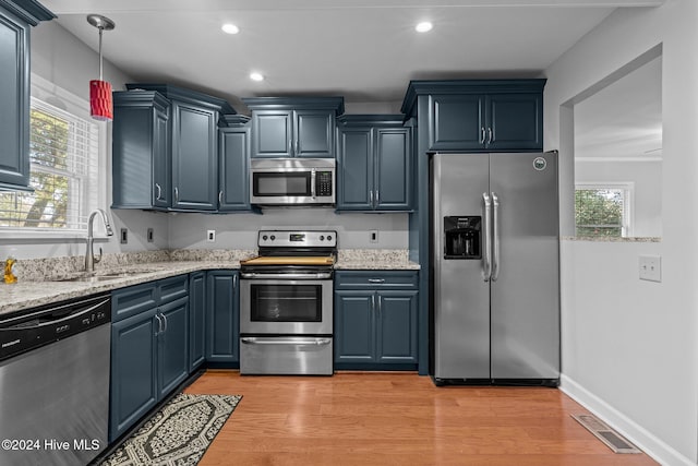 kitchen with pendant lighting, light hardwood / wood-style flooring, light stone countertops, blue cabinetry, and stainless steel appliances