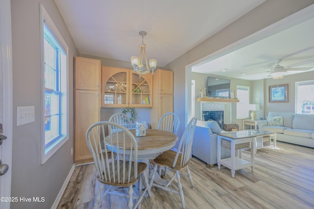 dining area with light hardwood / wood-style flooring, ceiling fan with notable chandelier, and a brick fireplace