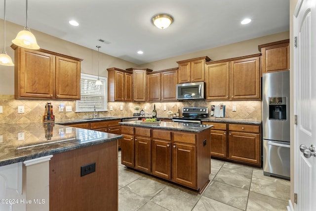 kitchen with pendant lighting, appliances with stainless steel finishes, a center island, tasteful backsplash, and dark stone counters