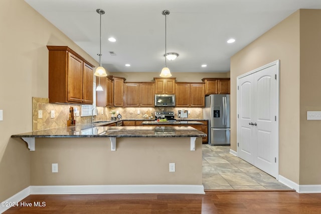 kitchen with pendant lighting, sink, dark stone countertops, stainless steel appliances, and kitchen peninsula