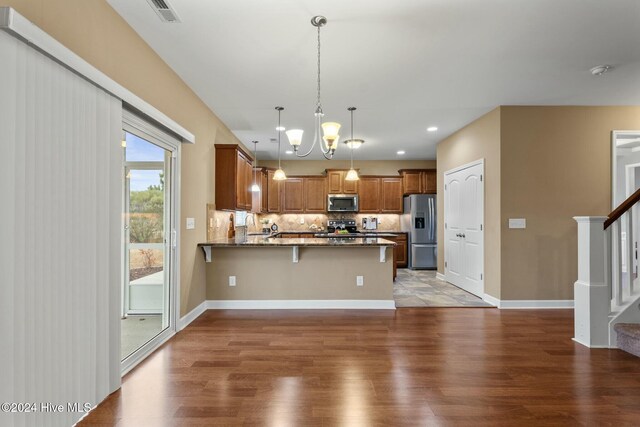 kitchen featuring tasteful backsplash, wood-type flooring, decorative light fixtures, appliances with stainless steel finishes, and kitchen peninsula