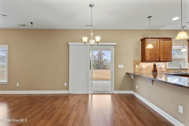 kitchen with pendant lighting, backsplash, dark hardwood / wood-style flooring, dark stone counters, and a notable chandelier