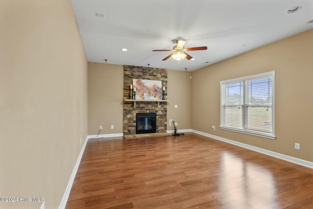 unfurnished living room featuring ceiling fan, a stone fireplace, and light wood-type flooring