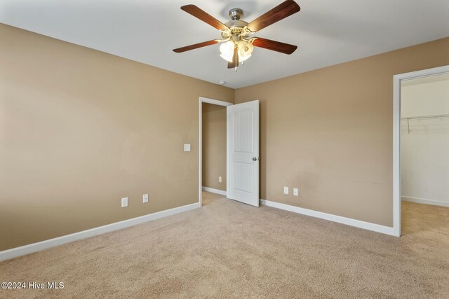 unfurnished bedroom with a spacious closet, light colored carpet, ceiling fan, and a closet