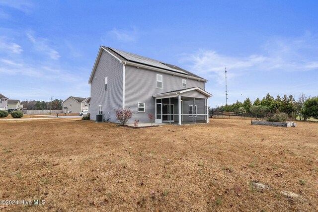 back of house with a sunroom, a yard, central air condition unit, and solar panels