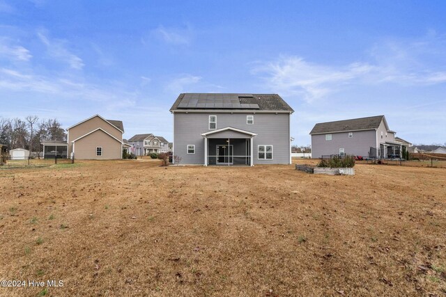 rear view of house featuring a lawn, a sunroom, and solar panels