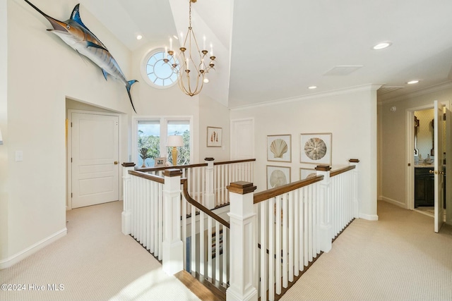 hallway with crown molding, a towering ceiling, light colored carpet, and an inviting chandelier