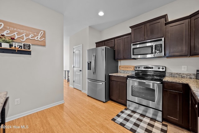 kitchen with dark brown cabinets, light hardwood / wood-style floors, light stone countertops, and appliances with stainless steel finishes