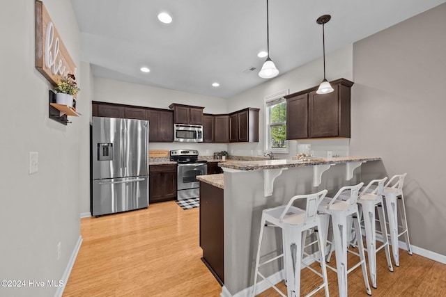 kitchen with dark brown cabinetry, hanging light fixtures, stainless steel appliances, kitchen peninsula, and a kitchen bar