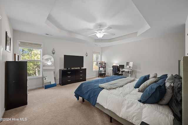 carpeted bedroom featuring a raised ceiling, multiple windows, and ceiling fan