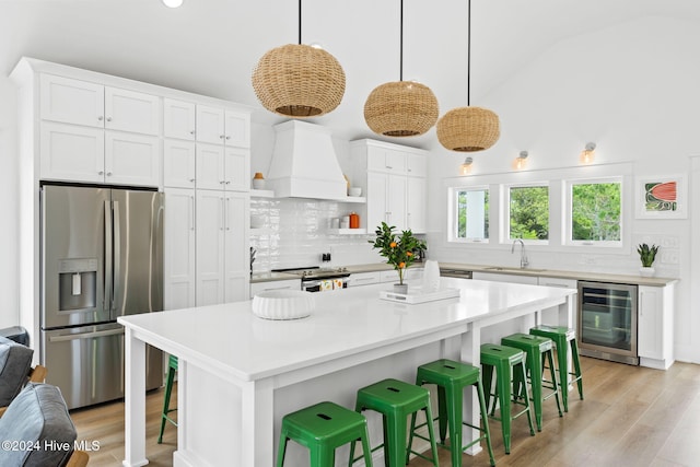 kitchen with premium range hood, white cabinetry, beverage cooler, and stainless steel appliances