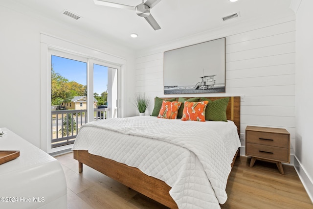 bedroom featuring access to exterior, ceiling fan, hardwood / wood-style floors, and wooden walls