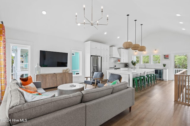 living room featuring vaulted ceiling, hardwood / wood-style flooring, wine cooler, and an inviting chandelier