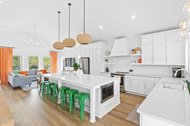 kitchen with a center island, light wood-type flooring, custom range hood, white cabinetry, and stainless steel appliances