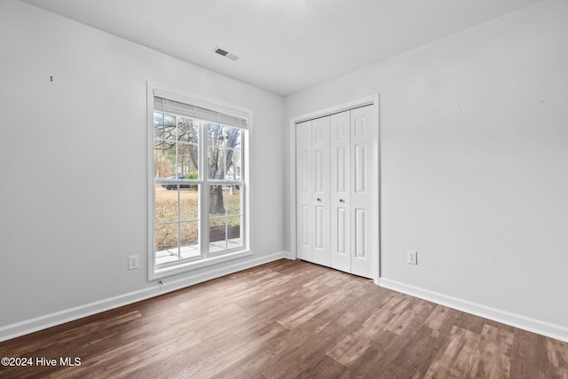 unfurnished bedroom featuring hardwood / wood-style flooring, multiple windows, and a closet