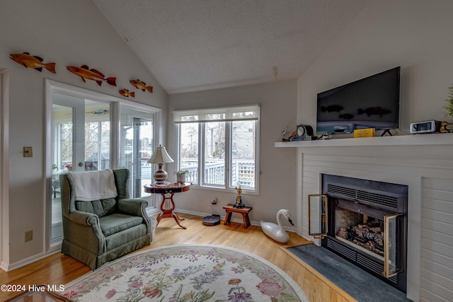 living area featuring a fireplace with flush hearth, vaulted ceiling, wood finished floors, baseboards, and a textured ceiling