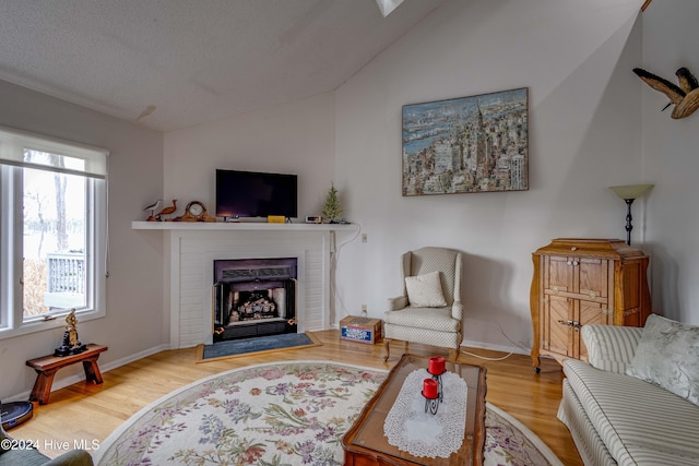 living room featuring vaulted ceiling, a brick fireplace, wood finished floors, and baseboards