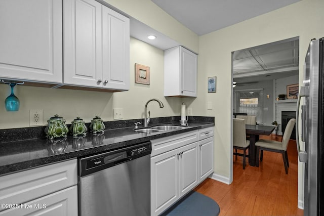 kitchen featuring sink, light hardwood / wood-style flooring, dark stone counters, white cabinets, and appliances with stainless steel finishes