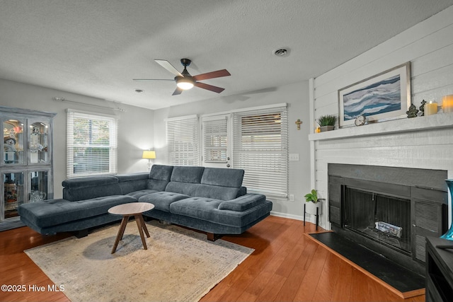 living room featuring ceiling fan, wooden walls, a textured ceiling, and hardwood / wood-style flooring